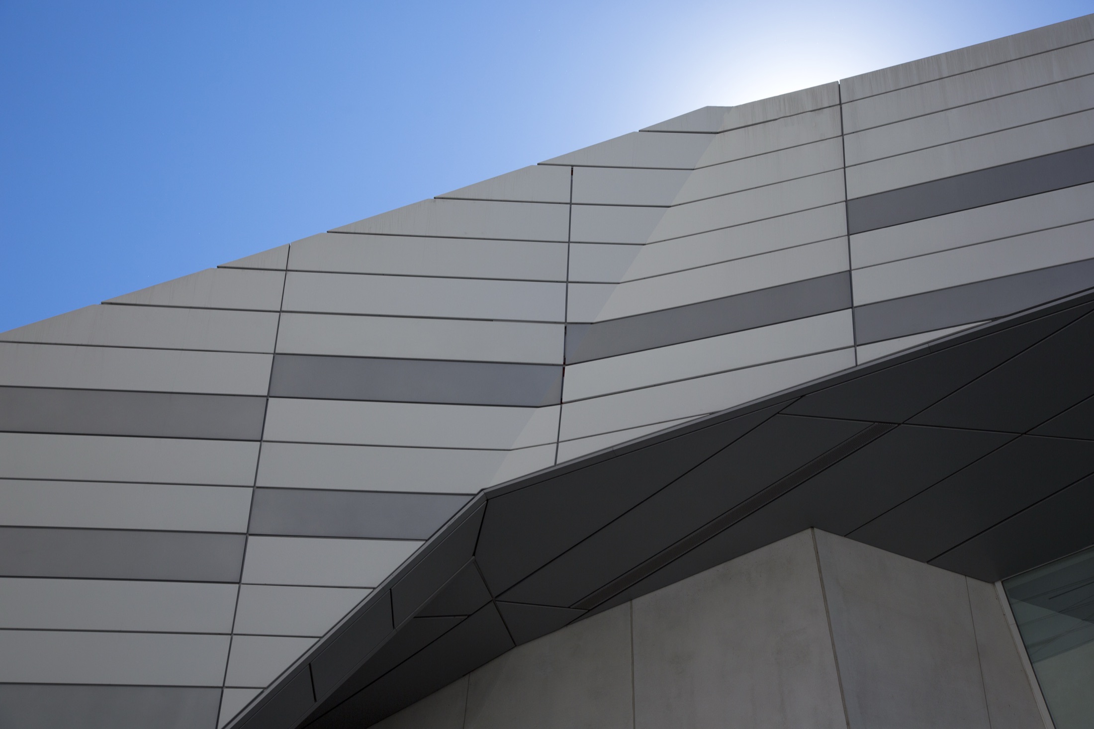 An angled view up a building facade clad in large panels against a clear sky.