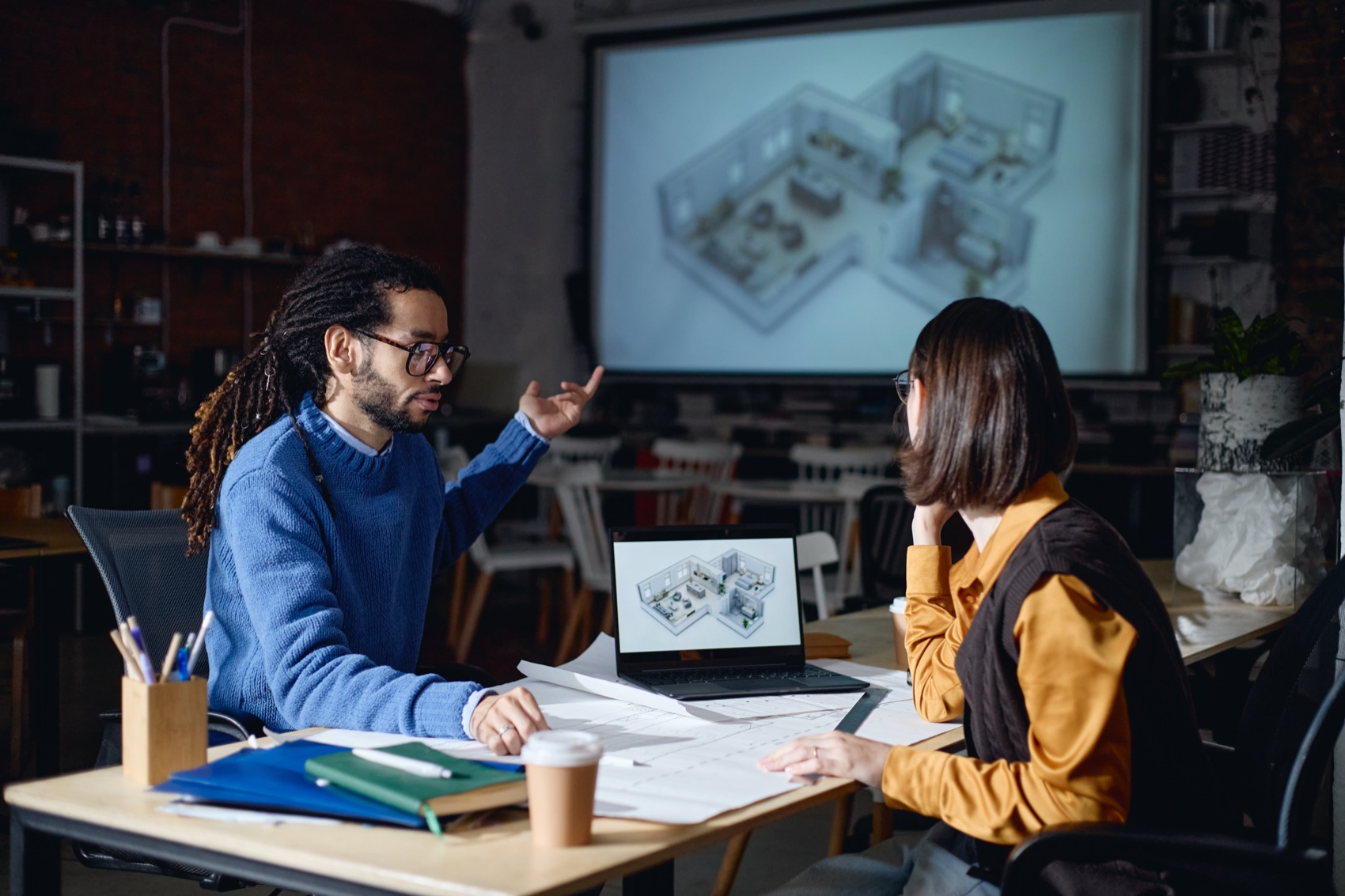 Two people discussing a three-dimensional floor plan shown on a screen and a laptop.